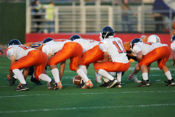 High school football players in their play stance at the line of scrimmage during a football game